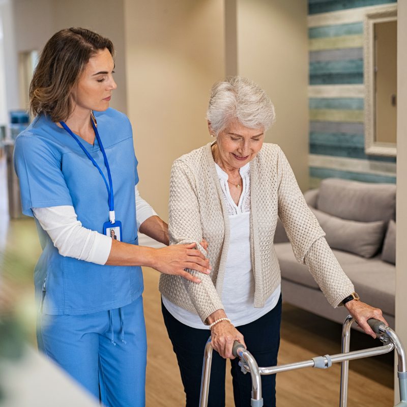 A nurse supporting a resident walking with a frame