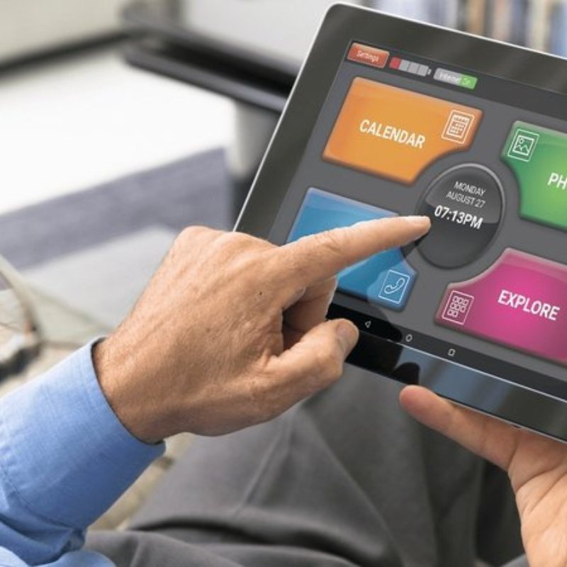 A person tapping the tablet home screen, with four large choices: Calendar, Photos, Talk and Explore